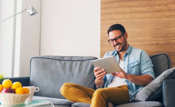 Junger Mann sitzt auf dem Sofa und freut sich über Content am Tablet
